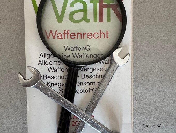 Eine Lupe und zwei gekreuzte Schraubenschlüssel liegen auf einem Dokument zum Waffenrecht. Unter der Lupe ist der Schriftzug „Waffenrecht“ zu erkennen.