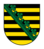 Wappen des Freistaats Sachsen mit schwarzen und goldenen Querstreifen sowie grünem Rautenkranz diagonal über dem Schild.