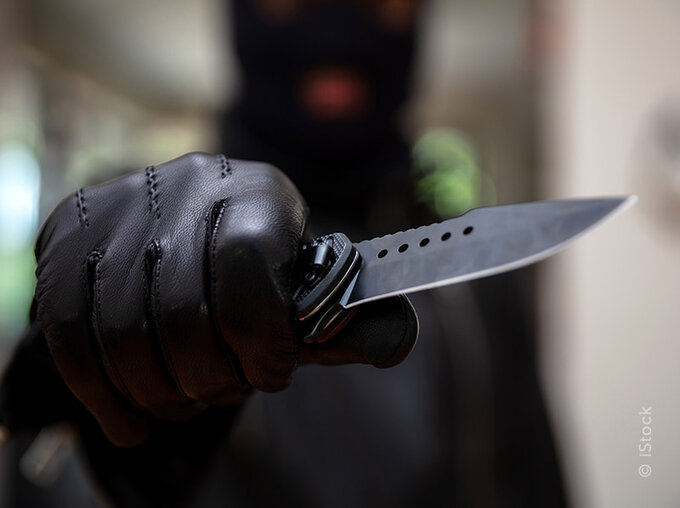 Hand in schwarzem Handschuh hält ein aufgeklapptes Messer; symbolisches Bild zum Thema Messergewalt und Messerverbot, unscharfer Hintergrund.